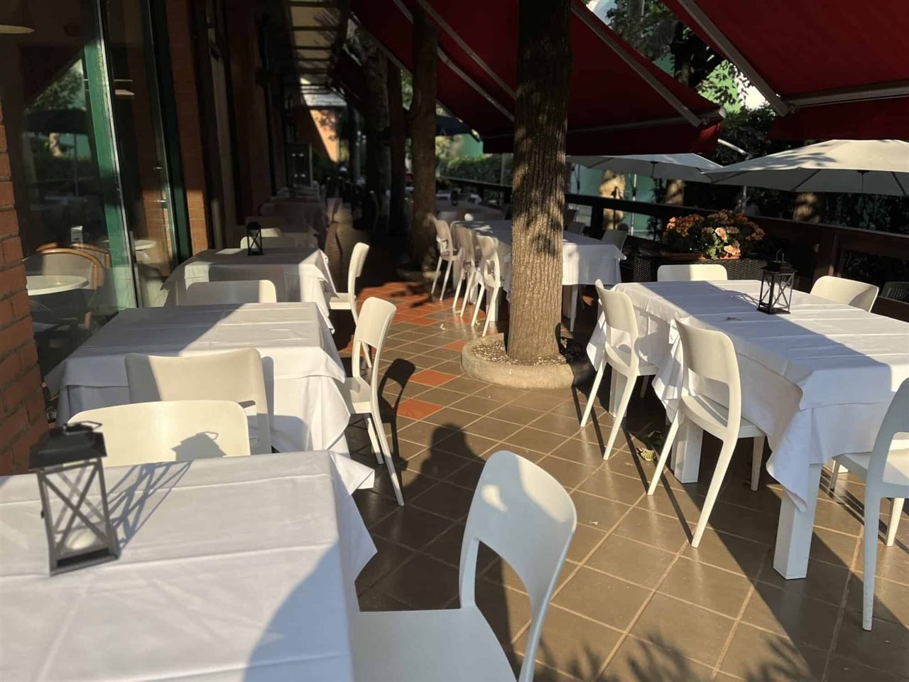 La veranda estiva del ristorante: tavoli all'aperto tra il verde, con le tende rosse del circolo